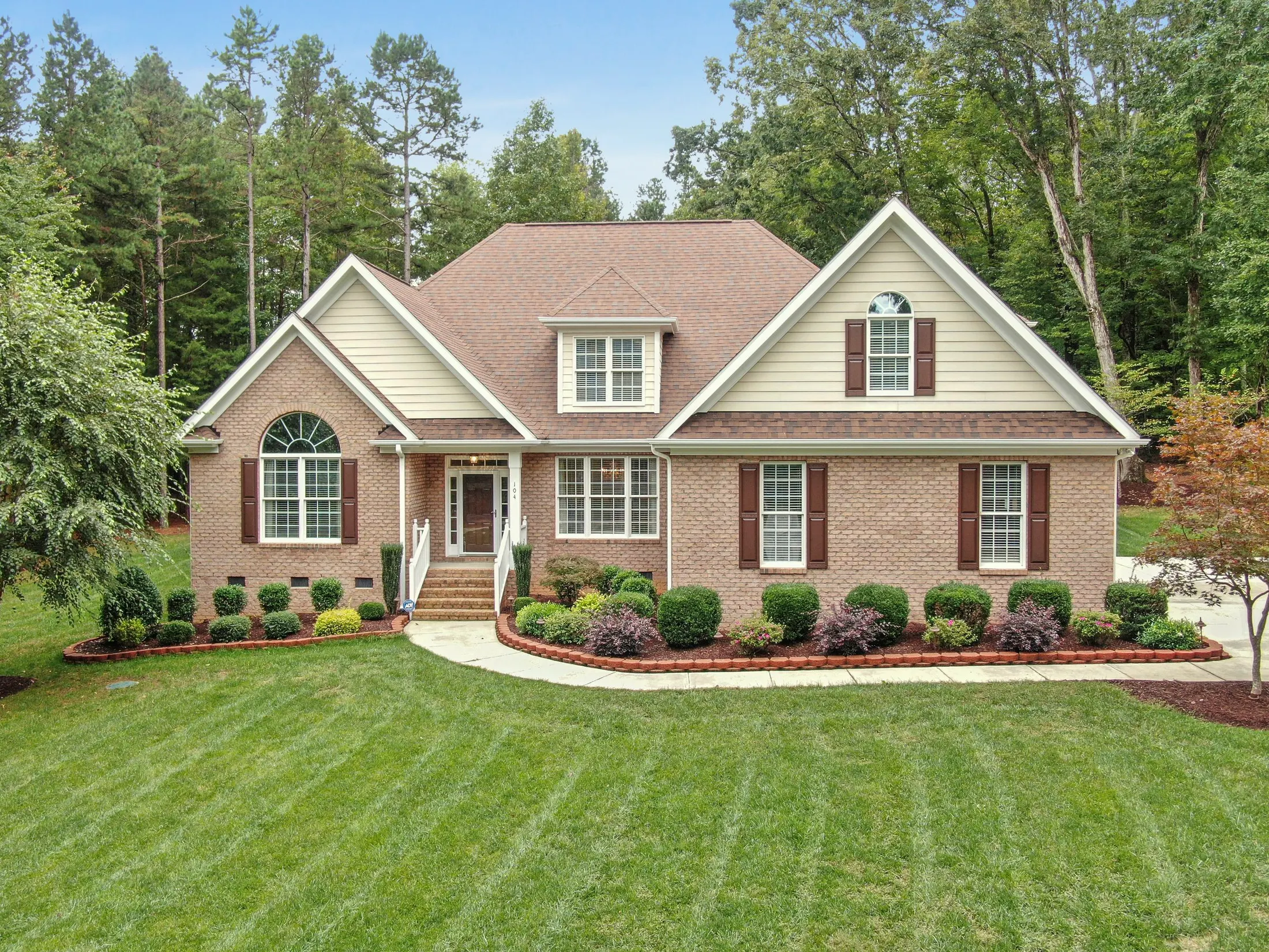 Red-brick two-story house with white trim, gabled roof and a front stoop behind a mowed lawn and trimmed shrubs