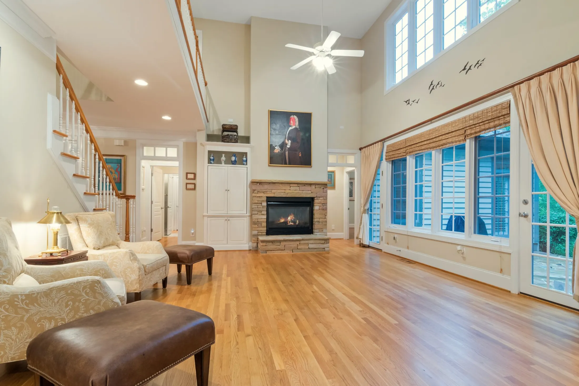 Great room with tall upper windows, a fireplace, a staircase and a hardwood floor