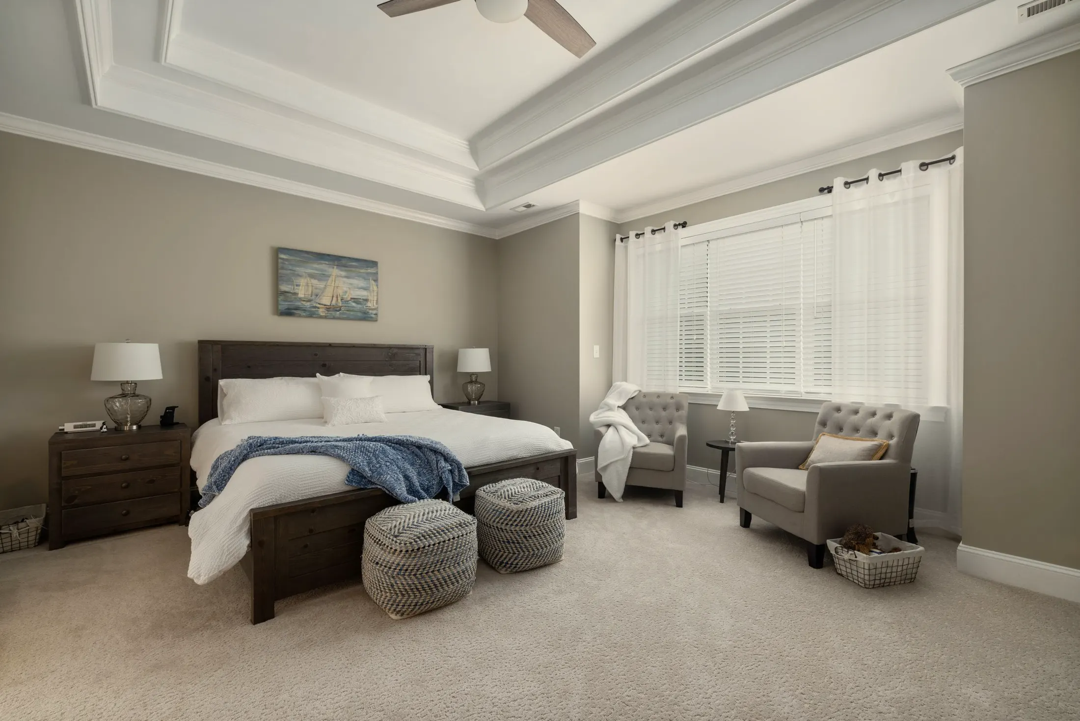 Primary bedroom with a tray ceiling, a dark wood bed and a sitting area by the windows