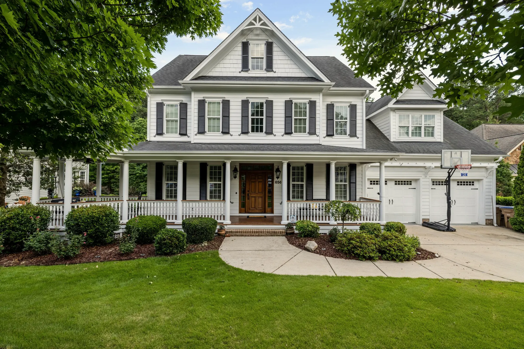 White two-story house with dark shutters, a covered front porch and a garage, behind a manicured lawn