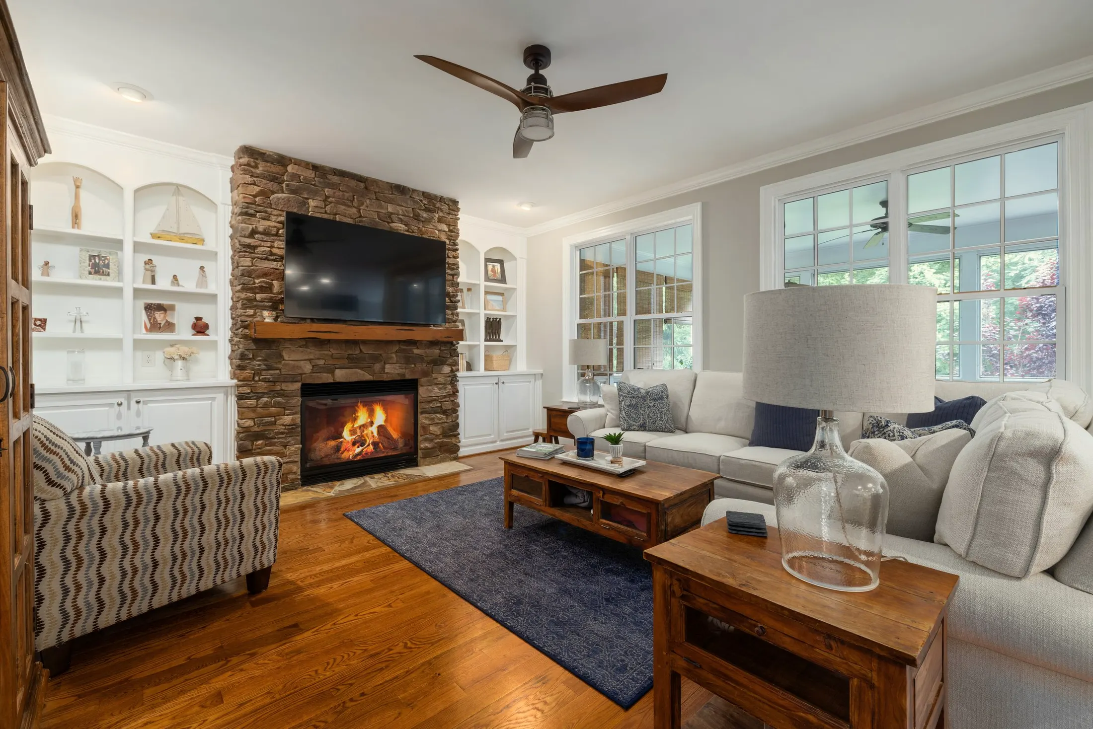 Living room with a stone fireplace, built-in shelves, a patterned rug and hardwood floors