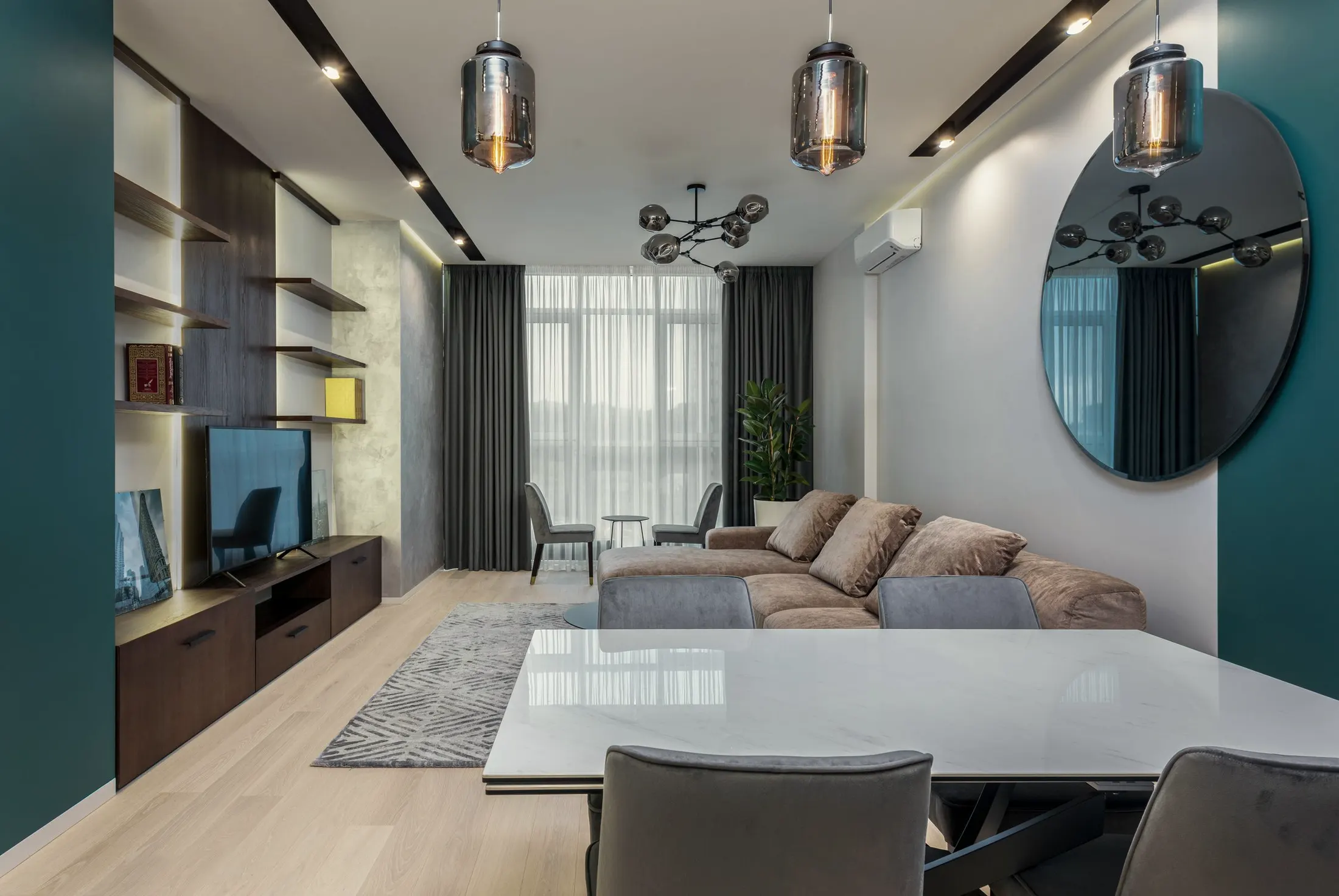 Living room with a television on a wooden console, a teal wall and sheer curtains over tall windows