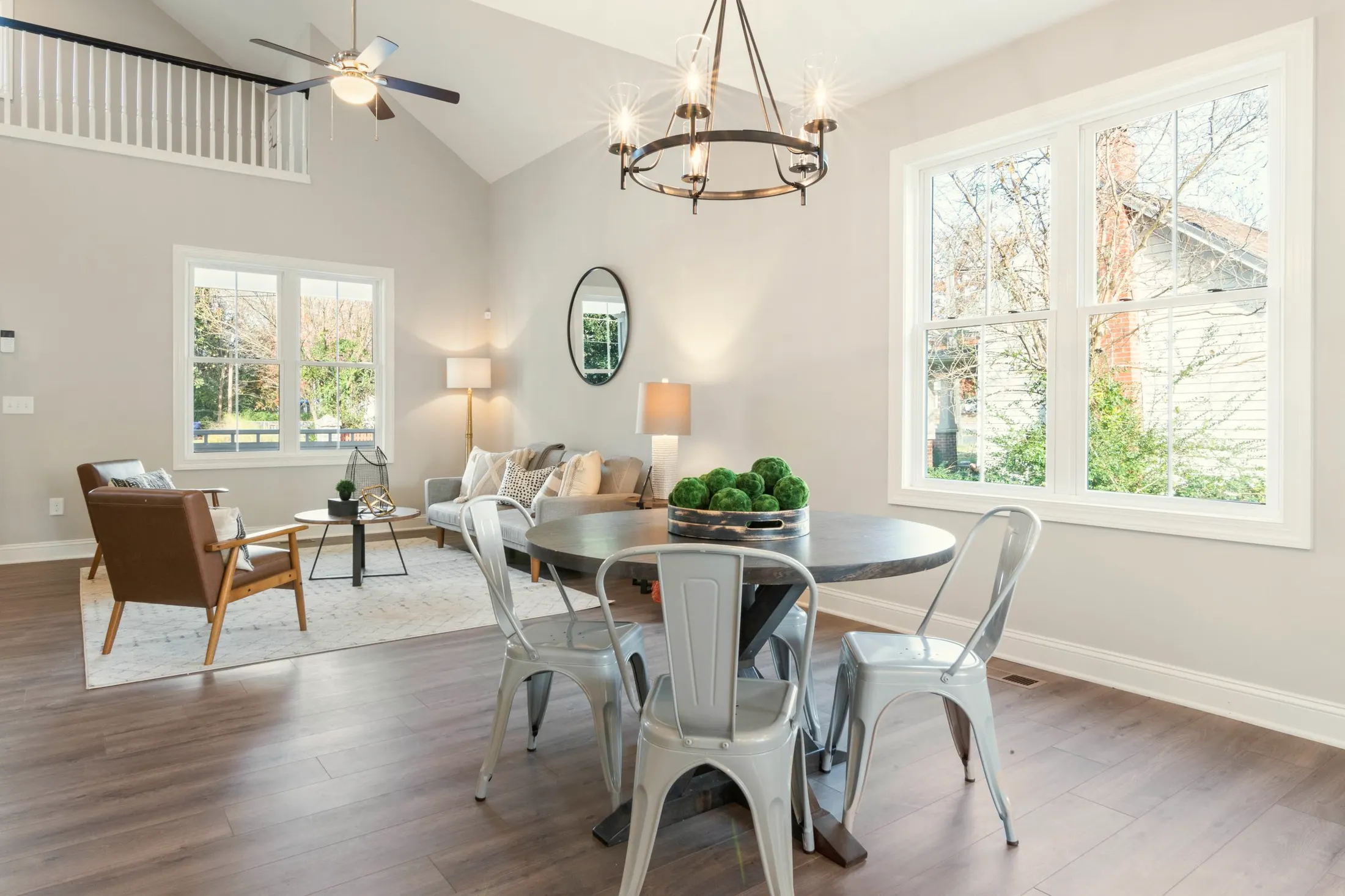 Round dining table with metal chairs under a black chandelier beside large windows