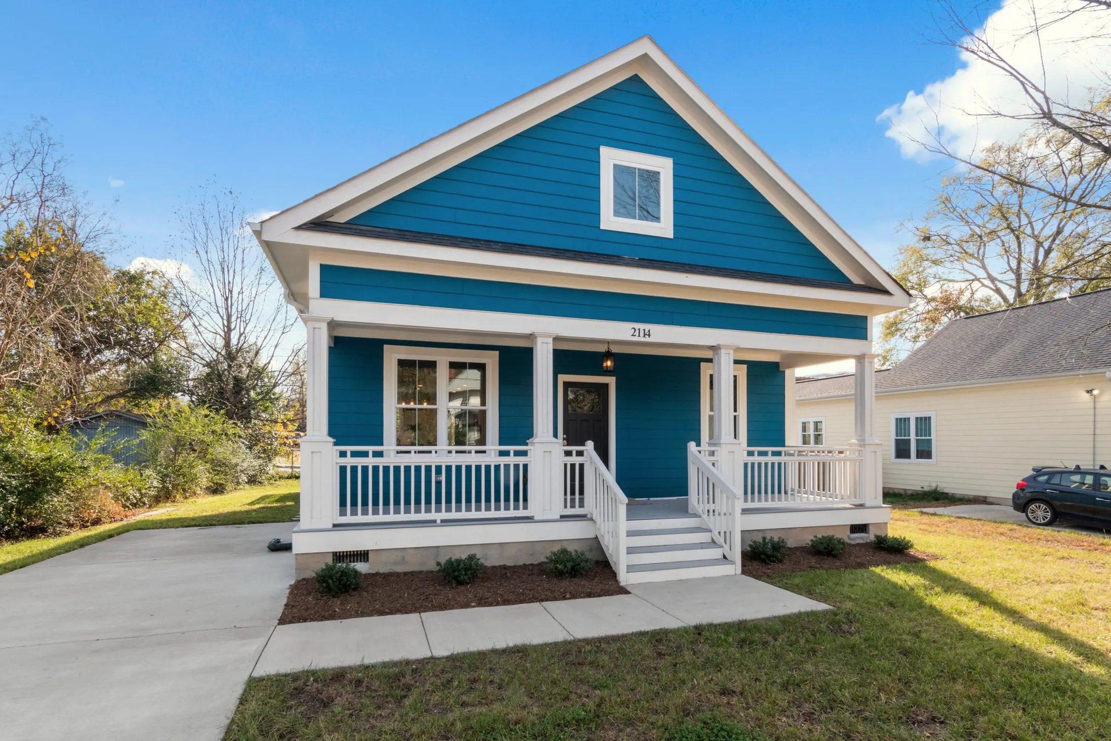 Blue craftsman cottage with white trim, a gabled dormer and a railed front porch with steps