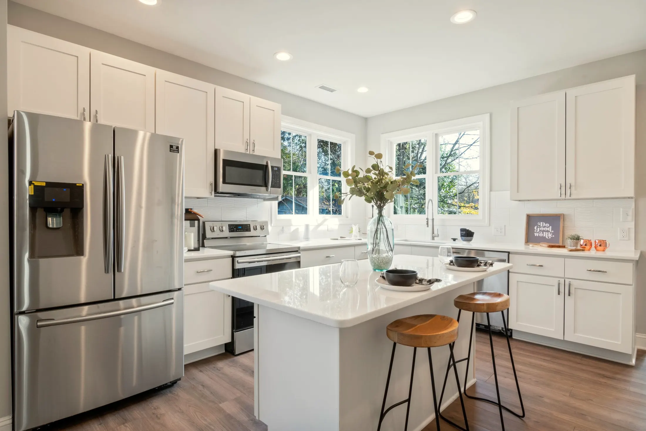 White kitchen with an island, two wooden stools and a stainless steel refrigerator