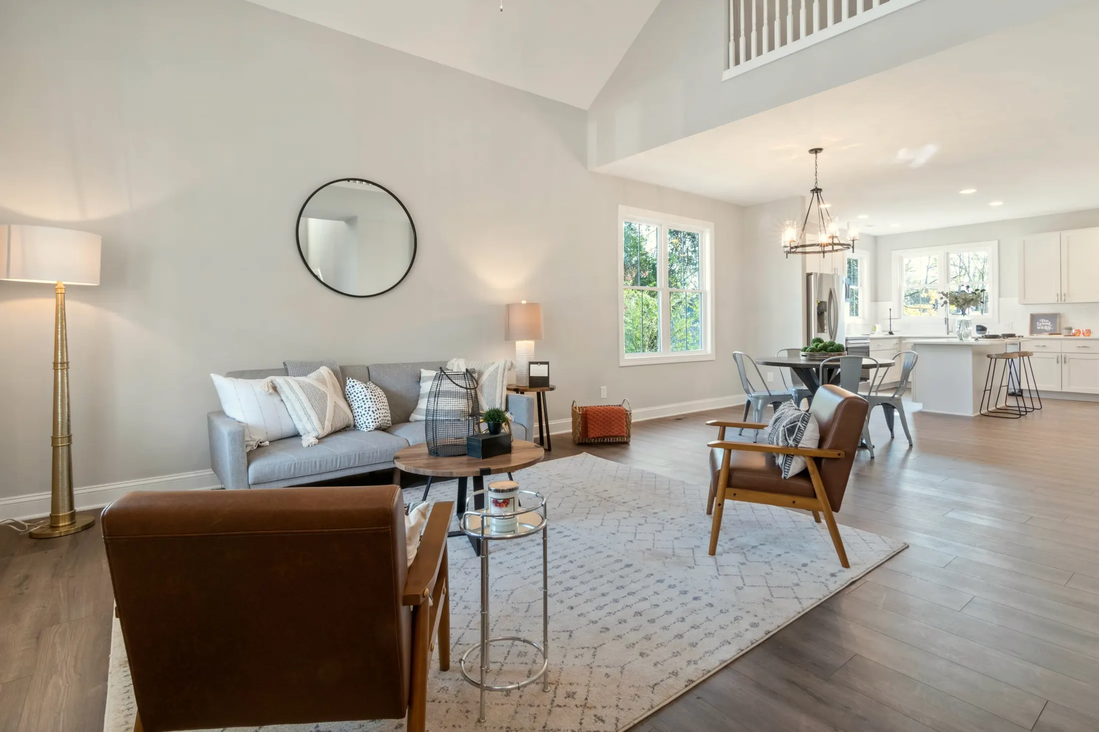 Tall living room with a gray sofa, leather armchair and a balcony rail overhead, opening to the dining area