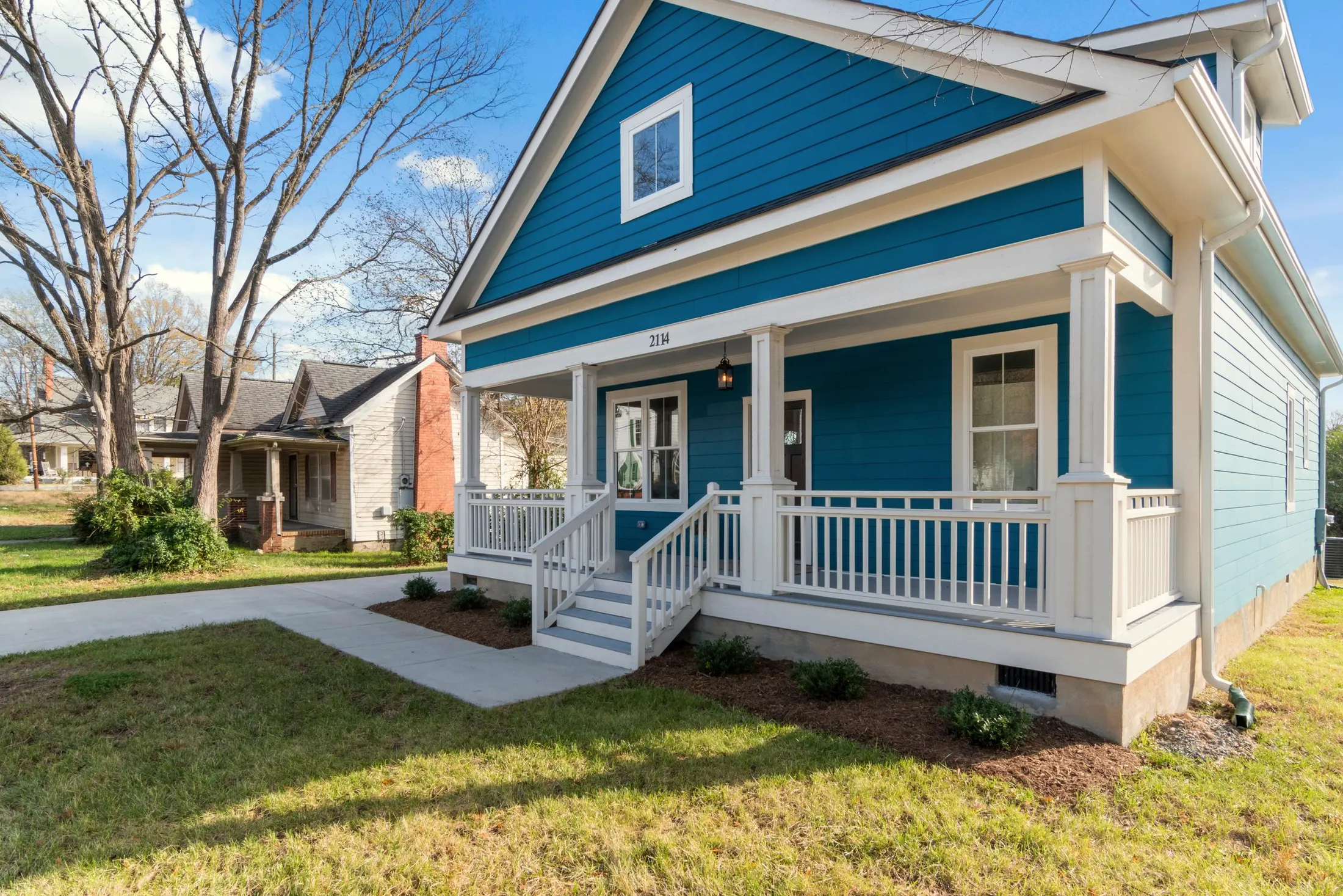 Front porch with white railings and steps, seen from the lawn at an angle