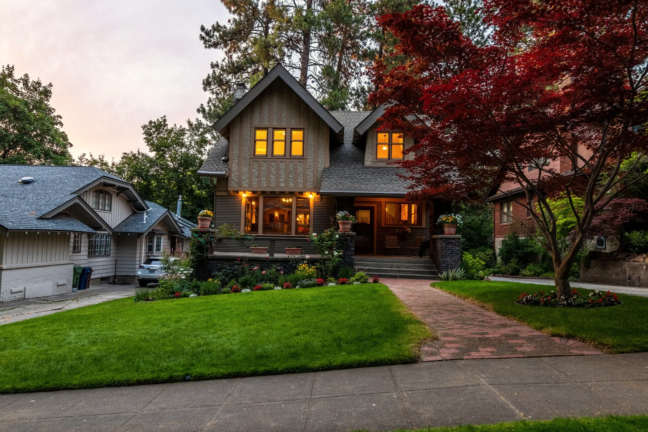 Craftsman house at dusk with warm lit windows, a brick path and a red maple on the lawn