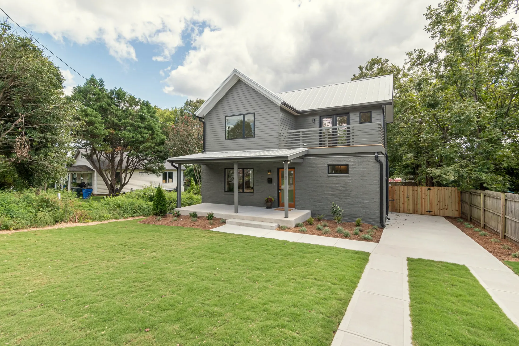 Gray two-story home with a covered front porch, black-framed windows and a balcony above, behind a green lawn