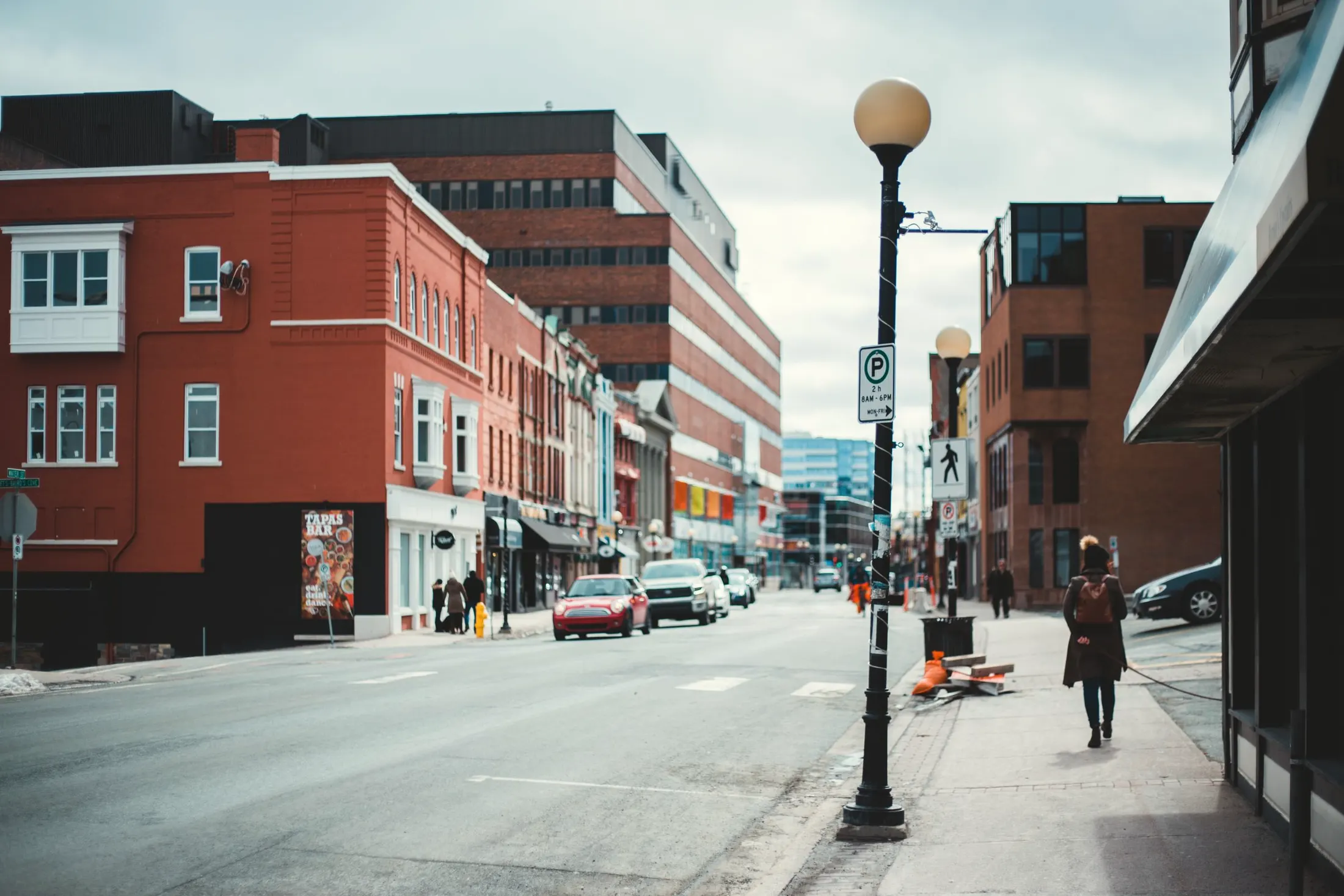 A city street with red-brick buildings, a lamp post and cars parked along the curb