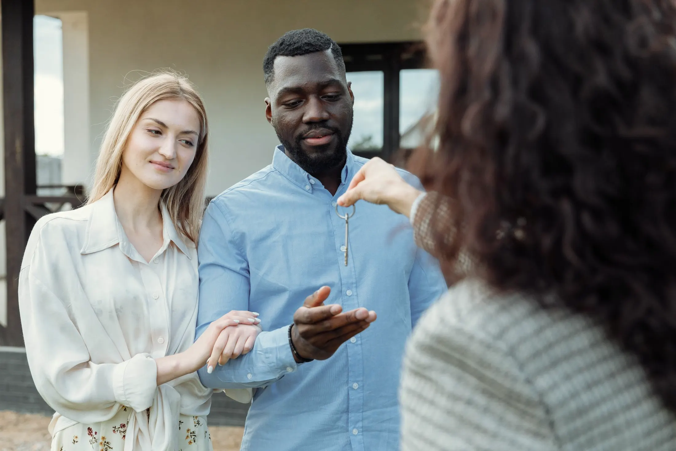 A couple being handed the keys to a home by an agent, standing outside the front door