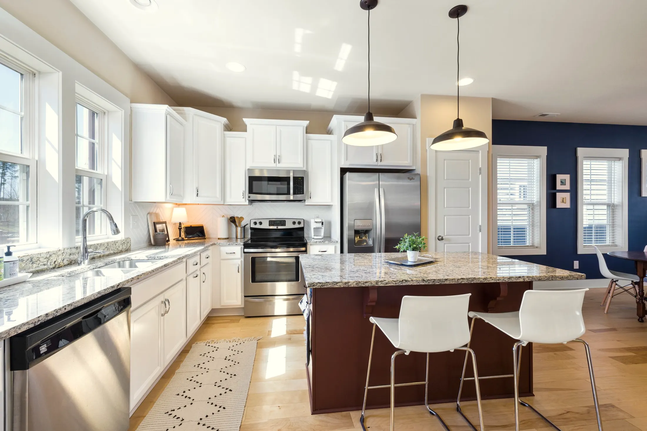 Kitchen with white cabinets, granite counters, stainless appliances and an island with two white stools