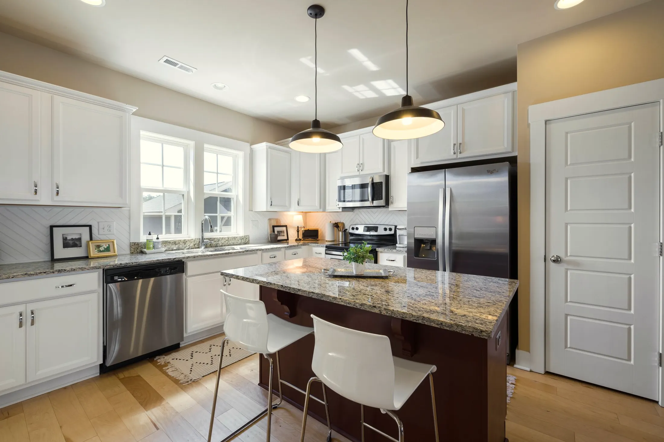 Kitchen island with granite top and stools in front of white cabinets and a stainless refrigerator