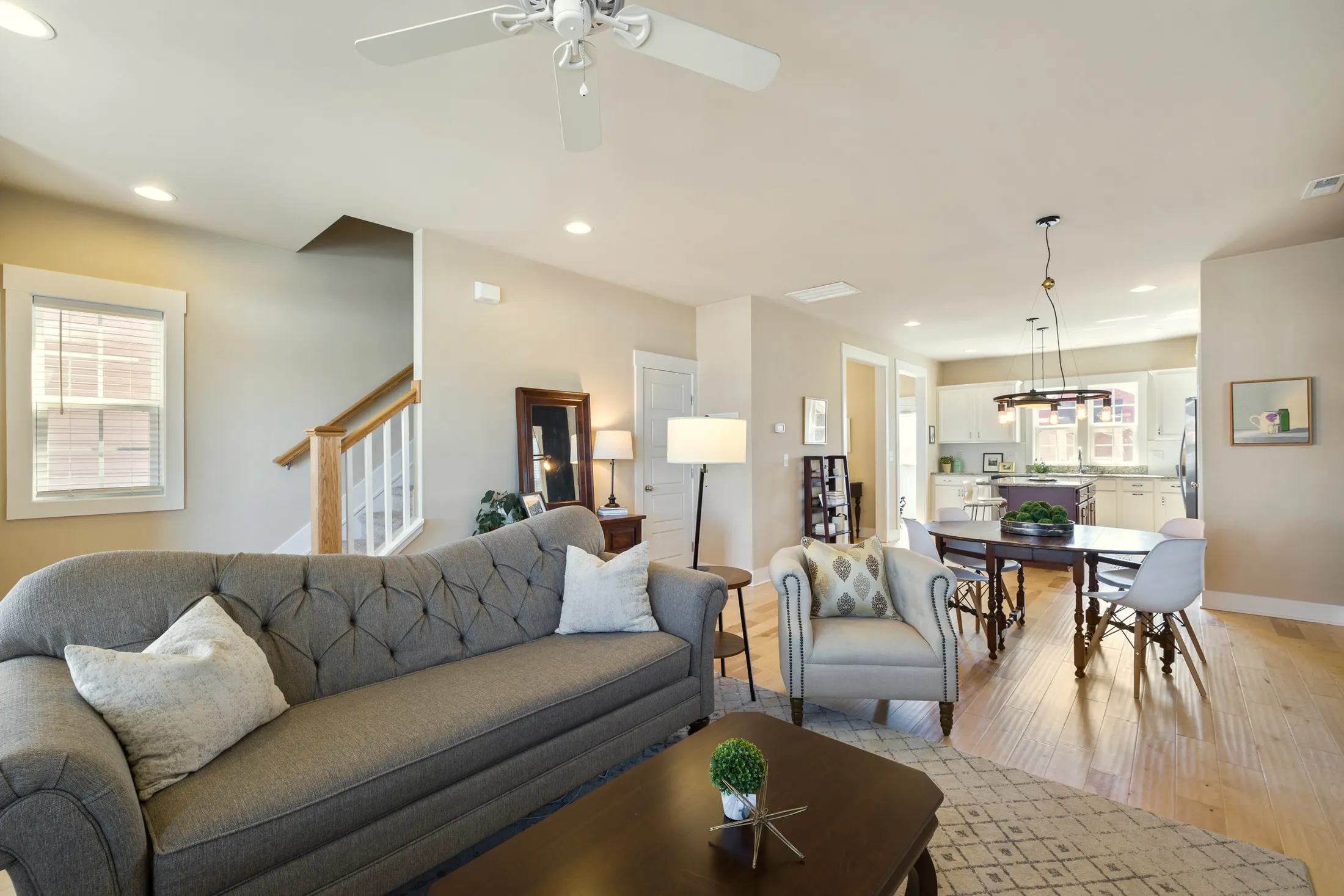 Sitting area with a gray tufted sofa, an armchair and a wooden coffee table beside the stairs
