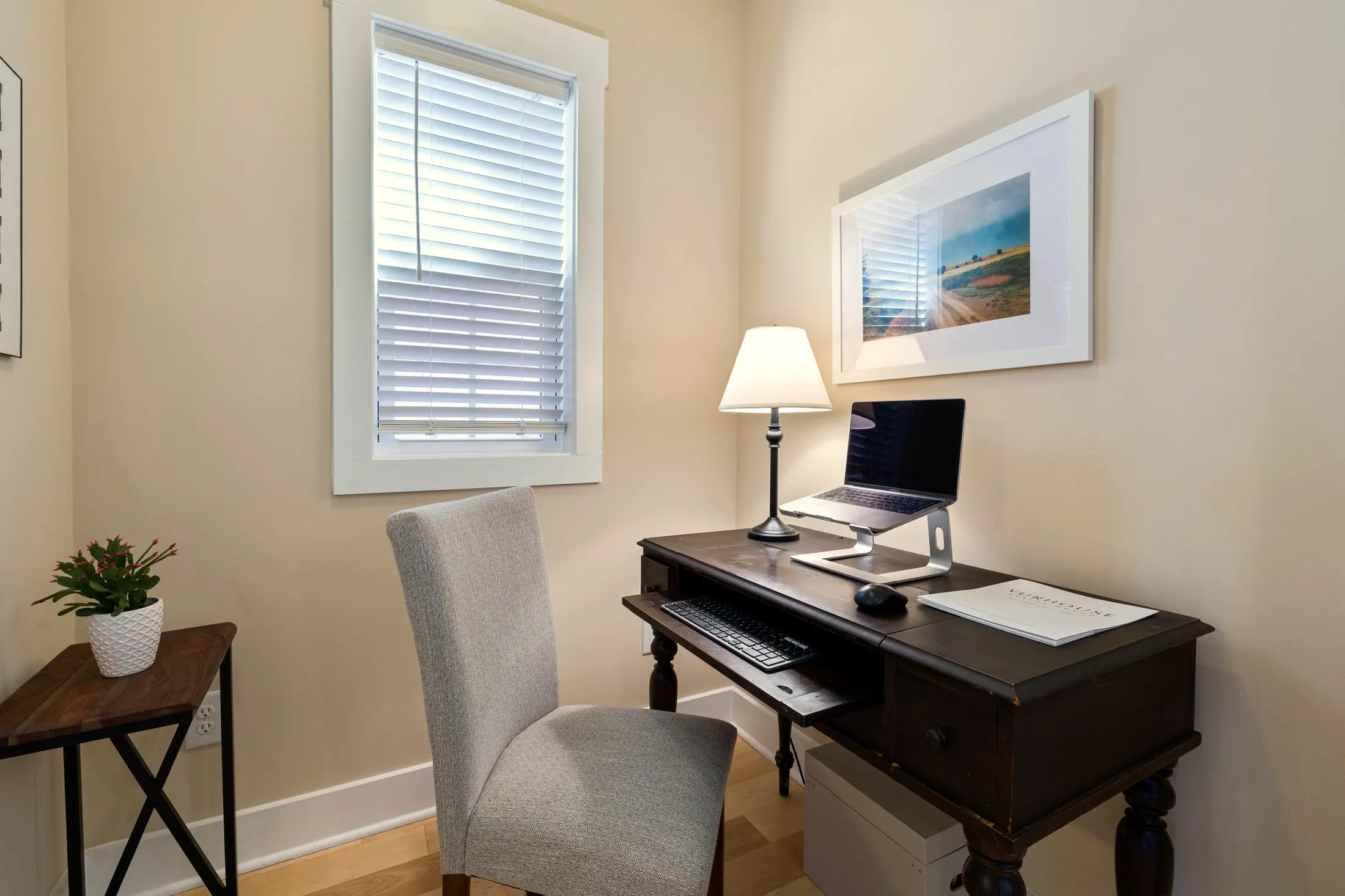 Home office with a dark-wood desk, a gray chair and a framed print by a window